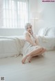 A woman sitting on a bed in a white room.