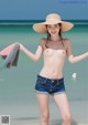 A woman in a straw hat and denim shorts on the beach.