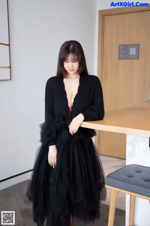 A woman in a black dress standing next to a table.