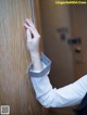 A woman in a white shirt is touching a wooden door.