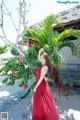 A woman in a red dress standing next to a palm tree.