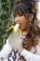 A woman eating a banana in front of a bush.