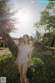 A woman in a striped bathing suit standing next to a tree.