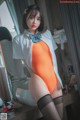 A woman in an orange bodysuit and black stockings posing for a picture.