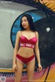 A woman in a red bikini standing in front of a graffiti wall.